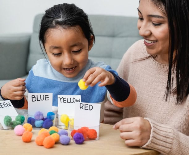 Child Coloring In Classroom With Teacher Support