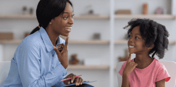 Teacher Helping Student Read Book In Classroom