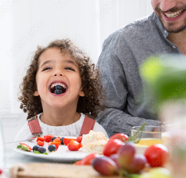 Playful boy with his father eating blueberries at table